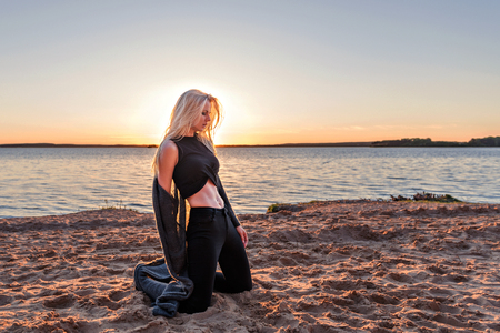 attractive sensual girl blonde with beautiful abdominal muscles kneeling on the beach with an expression of pleasure on her faceの写真素材