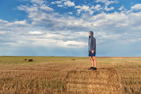 a young guy in a hood stands on a haystack in a wheat field after a rain with a storm sky on the...