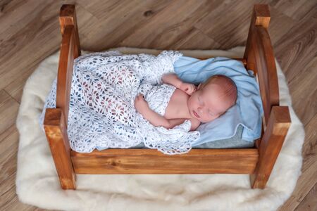 newborn lies in a wooden bed covered with a white blanketの写真素材