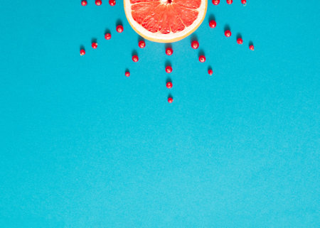 Sun made of red juicy grapefruit and cranberry on bright blue background. Creative summer design....