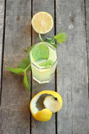 Top view of glass of lemonade with mint leaf in it, with mint twig, half cut lemon and lemon peel on tableの写真素材