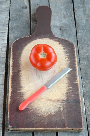 Tomato with red knife on old cutting boardの写真素材