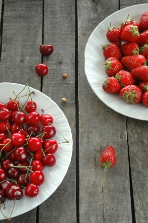 vertical diagonal composition of strawberries and sweet cherries on white plates, on old gray wood table,  in perspective の写真素材