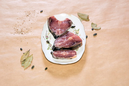 Red fish meat with laurel leaf and pumpkin seed in white dish on yellow paper