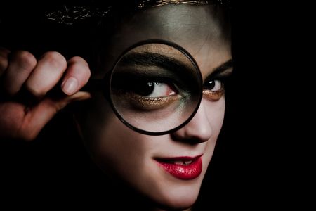 young woman with strange make up holding magnifying glass infront eyeの写真素材