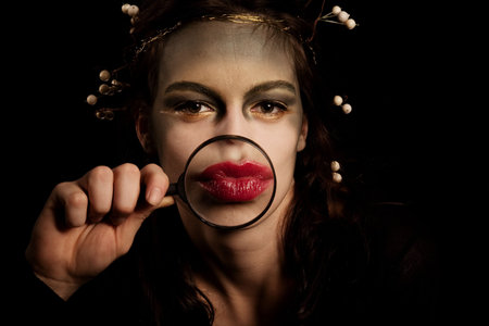 young woman with strange make up holding magnifying glass infront lips