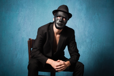 scary man in black suite with black mask and hat sit on chairの写真素材