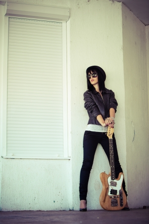 young woman in rock style clothes with electric guitar outdoor shotの写真素材