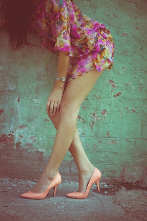 summer fashion woman with long slim legs in high heel shoes against wall outdoor shot retro colorsの写真素材