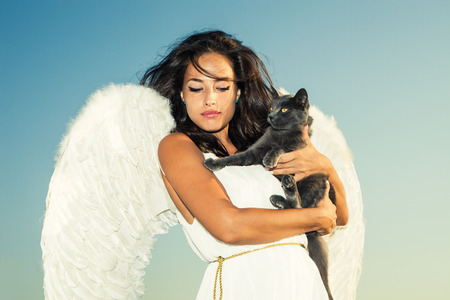 beautiful angel woman against sky with cat in her armsの写真素材