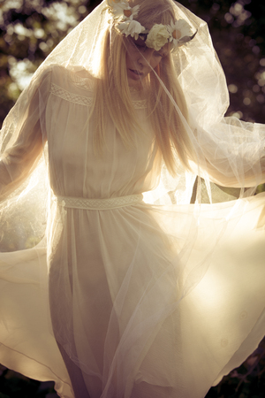 beautiful blonde woman with wreath of flowers and white veil summer portrait outdoorの写真素材