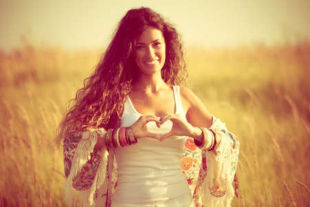 smiling young woman in summer field show heart shape hands signの写真素材