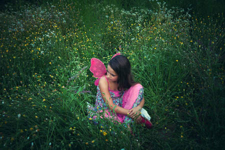 girl like a fairy sitting in meadow grass with pink wings shot from aboveの写真素材