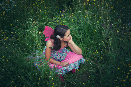 girl like a fairy sitting in meadow grass with pink wings shot from above