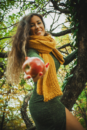 smiling young woman in park on tree offering an apple in hand, focus on faceの写真素材