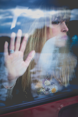 young woman portrait in the car behind the window, hand on glass looking awayの写真素材
