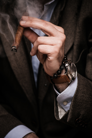 elegant man wearing suit and white shirt smoking  cigar indoor shot, closeup, selective focusの写真素材