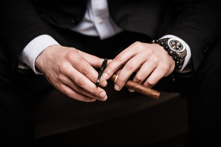 elegant man wearing black suit and white shirt cut Cuban cigar indoor shot, closeupの写真素材