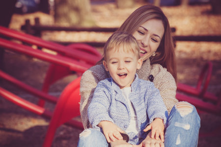 life is beautiful when you're a kid, child with his mother enjoy on roundabout in park, autumn day,...