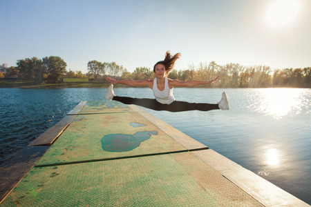 girl doing spaga in air by the lake,  sunny  autumn day, full body shotの写真素材