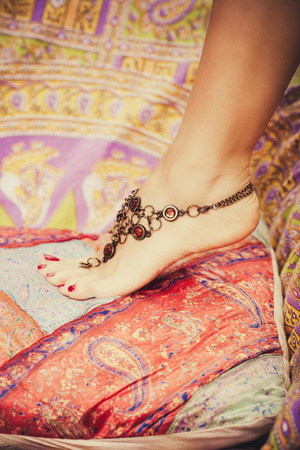 closeup of female foot with boho style foot jewelry on colorful pillows outdoor shot selective focusの写真素材