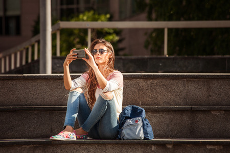 young urban woman in casual clothes sit on stairs take a photo with smartphoneの写真素材