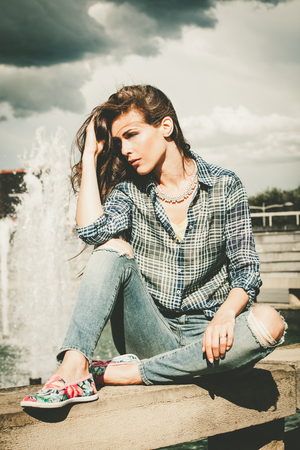 casual urban young woman sit by city fountain full body shotの写真素材