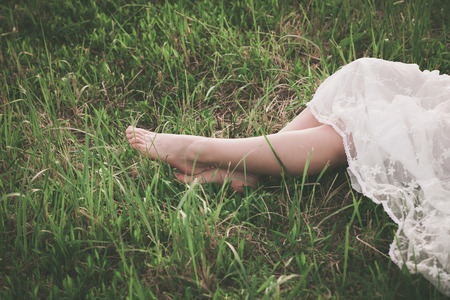 woman in white lacy dress barefoot legs on grass closeの写真素材