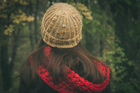 back view of woman with wool cap and scarf outdoor autumn winter day in wood closeup