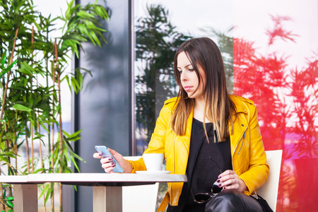urban girl sit in cafe outdoor with coffee checking messages on smartphone spring day city life conceptの写真素材