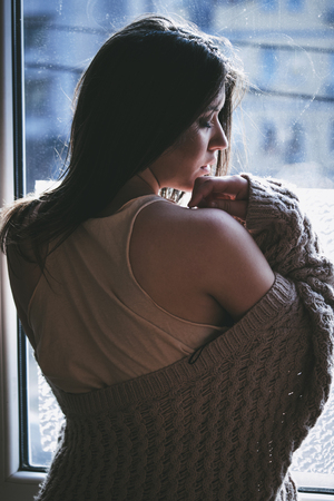 beautiful pensive young woman by the window portraitの写真素材