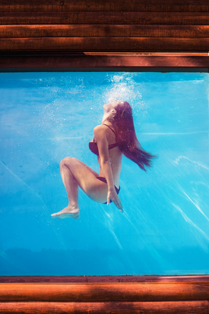 girl in bikini underwater in pool through the glass outdoor  summer dayの写真素材