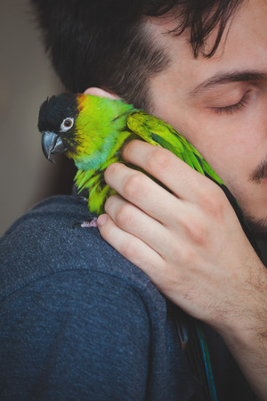 young man cuddle his pet parrot on shoulder  closeup indoor at homeの写真素材