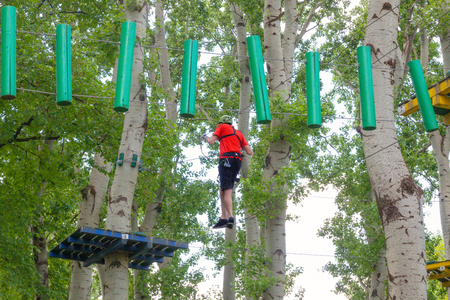 young man passes obstacles in adventure park in forestの写真素材