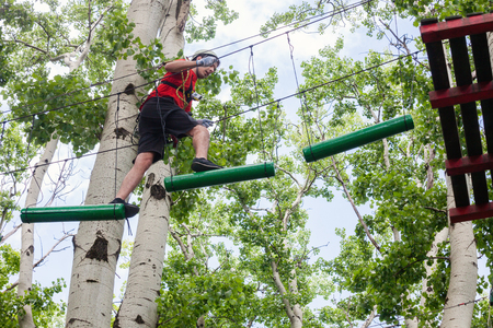 young man passes obstacles in adventure park in forestの写真素材