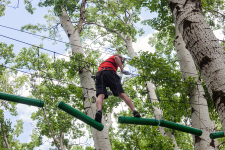 young man passes obstacles in adventure park in forestの写真素材