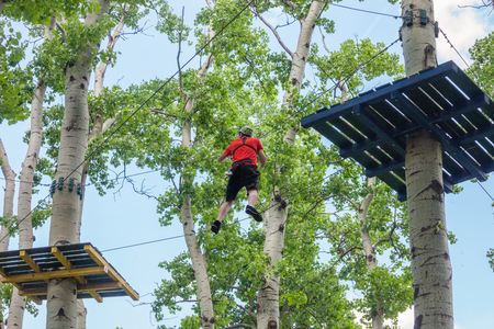 young man passes obstacles in adventure park in forestの写真素材
