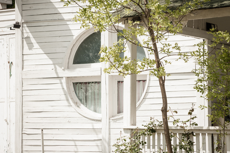 small white wooden house with round window and tree infrontの写真素材