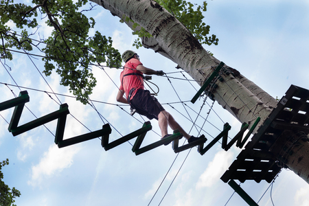 young man passes obstacles in adventure park in forestの写真素材