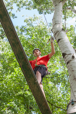 young man passes obstacles in adventure park in forestの写真素材