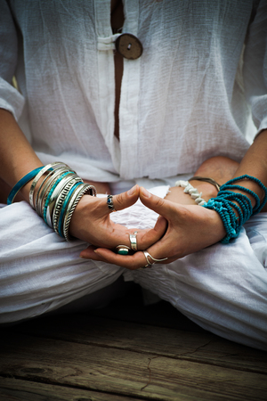 woman in a meditative yoga position outdoor  in white clothes wearing lot of bracelets and rings focus on hands in mudraの写真素材