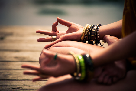 woman in a meditative yoga position sit on wooden pontoon on the lake wearing lot of bracelets and rings lower bodyの写真素材