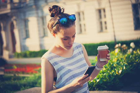 student girl in the city  streert using smartphone and drinking coffee wearin casual summer clothes and sunglasses on headの写真素材