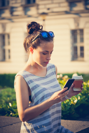 student girl in the city  streert using smartphone and drinking coffee wearin casual summer clothes and sunglasses on headの写真素材