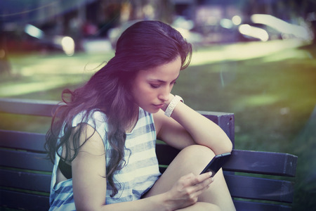 portrait of girl in city park using smartphone summer dayの写真素材