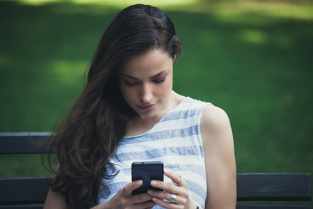 portrait of girl in city park using smartphone summer dayの写真素材