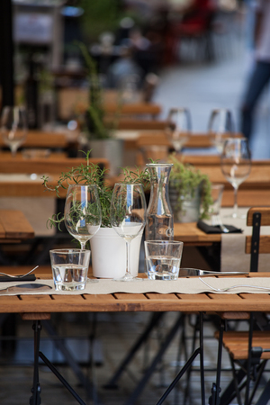 tastefully decorated wooden table in  restaurant outdoor with wine glasses, water and herbsの写真素材