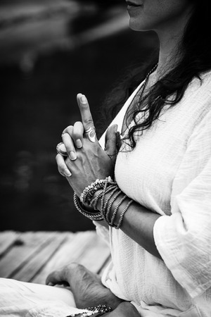 woman hands in yoga symbolic gesture mudra wearing lot of bracelets and rings outdoor closeup by the lake summer day bwの写真素材