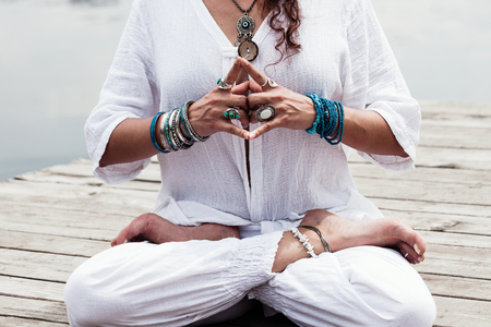 woman hand in yoga symbolic gesture mudra wearing lot of bracelets and rings outdoor closeup by the lake summer dayの写真素材