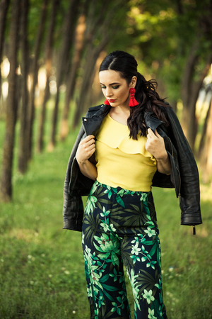 attractive black hair woman summer fashion look in yellow shitr pants and black leather jacket outdoor in city parkの写真素材